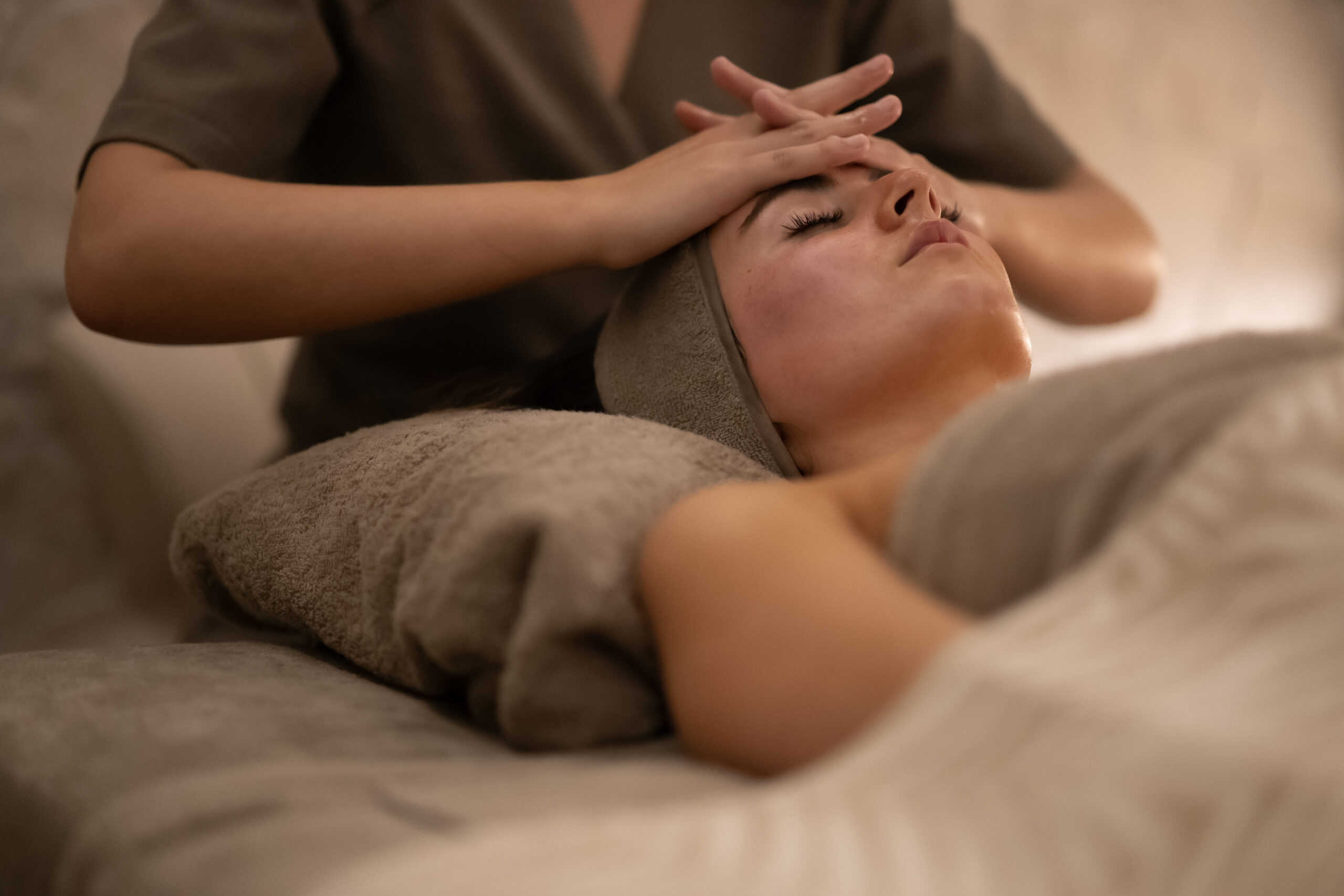 Person lying down with eyes closed as a therapist gently massages the scalp with both hands.