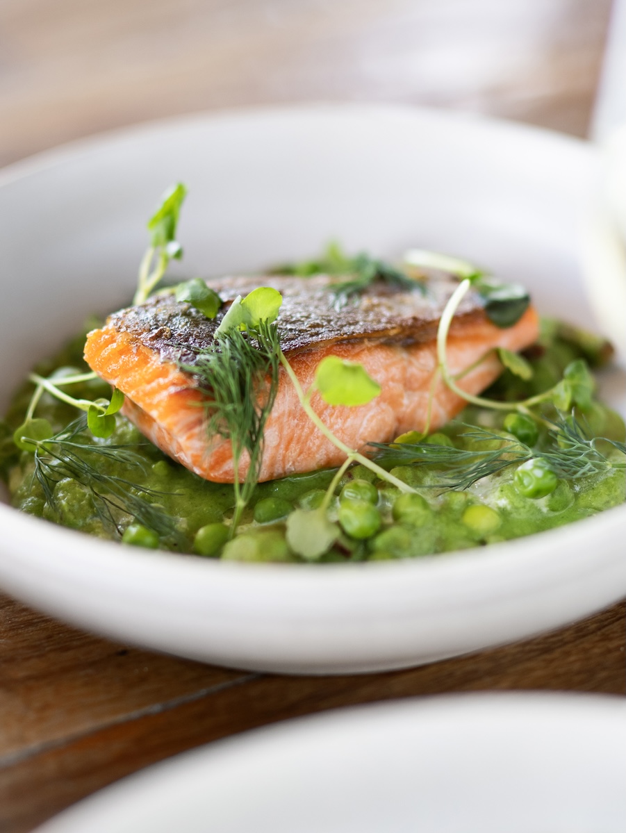 Pan-seared salmon fillet with crispy skin on a green pea purée, garnished with dill and microgreens.