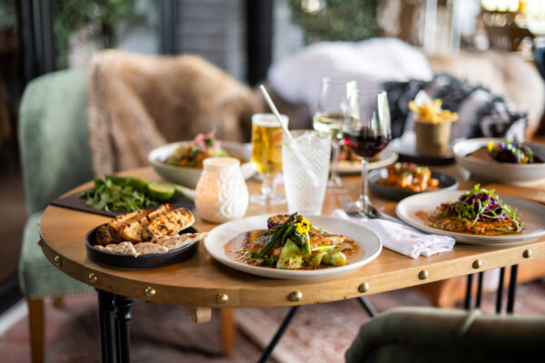Table set with multiple plated dishes, bread, and beverages in a cozy restaurant setting.