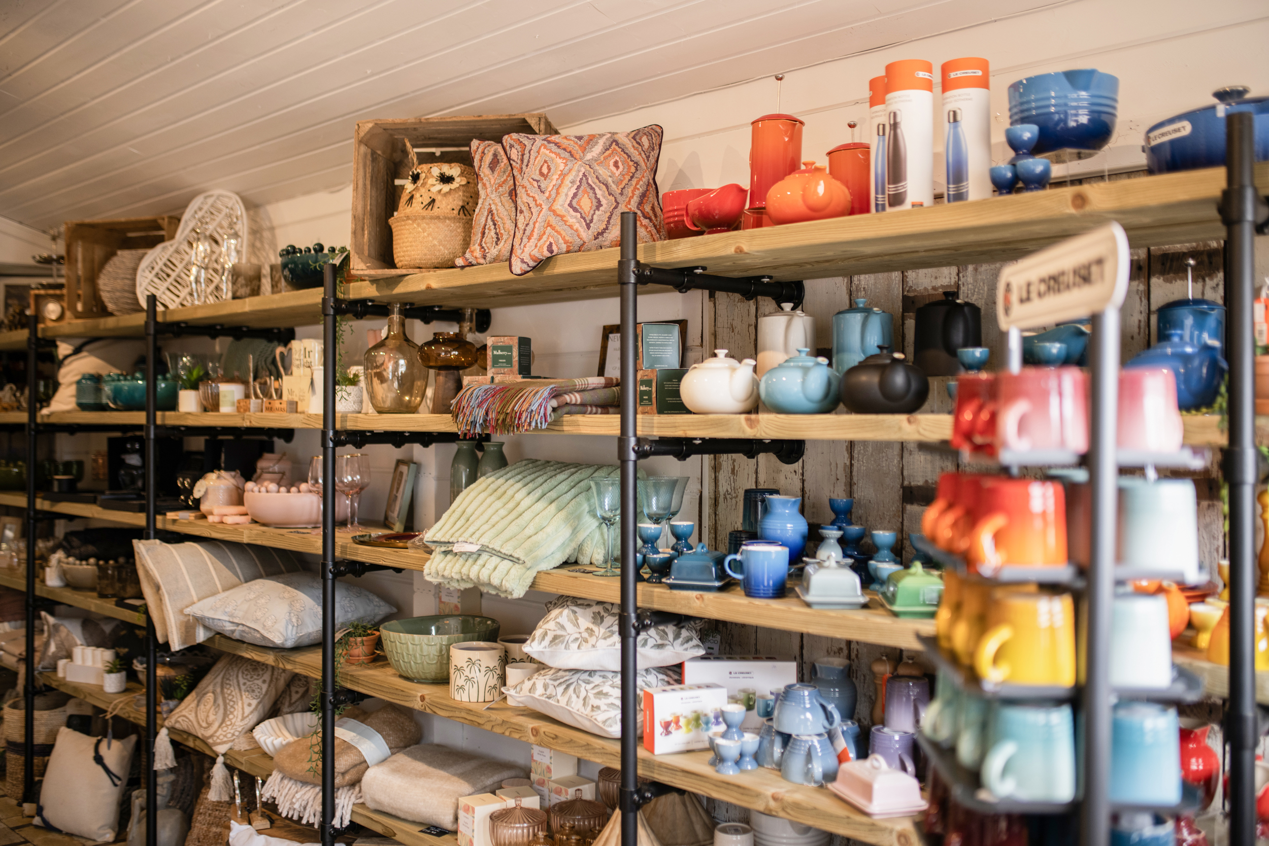 Shelf display of colorful ceramic bowls, teapots, and woven cushions in a home decor shop.